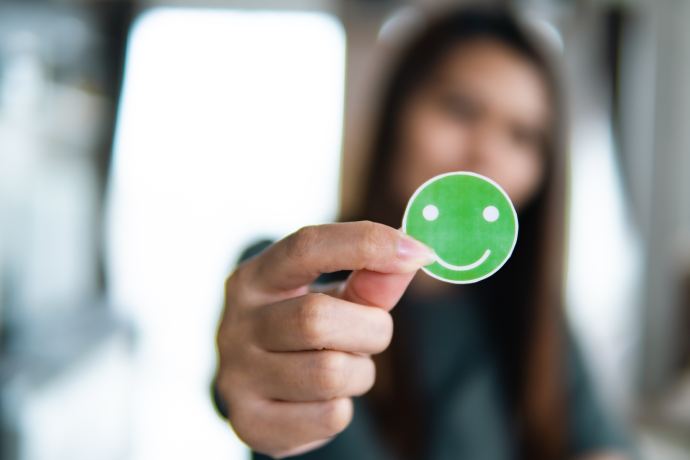Main tenant un autocollant smiley vert, satisfaction client DIAGOME